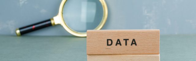 Conceptual of data analysis with wooden blocks, magnifying glass on sage color background side view. horizontal image